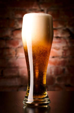 glass of lager on table against brick wallの写真素材