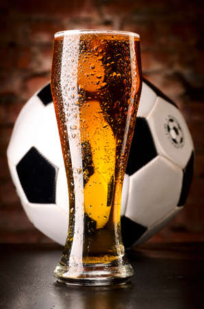 glass of lager with soccer ball on table against brick wallの写真素材
