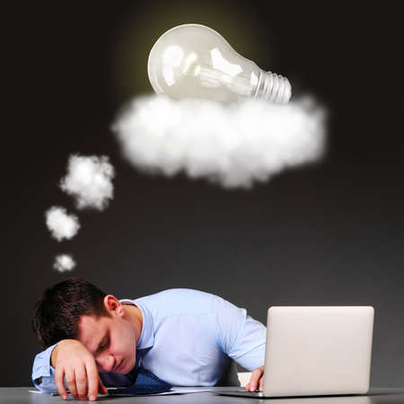 tired businessman is sleeping at his table with laptop and a bulb above his headの写真素材