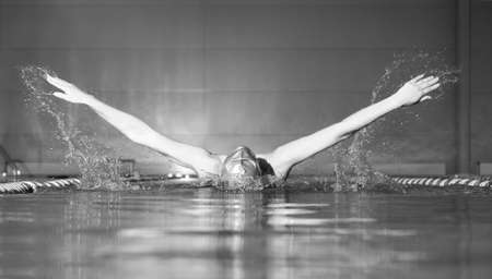 woman swims using the butterfly stroke in indoor poolの写真素材