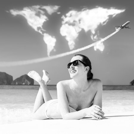 travelling  young woman is lying on beach under continents shaped cloudsの写真素材