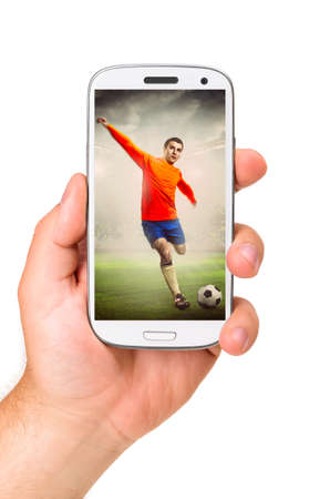 hand is holding a modern phone with soccer or football player shooting a ball on screenの写真素材