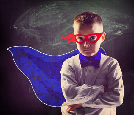 school boy wearing a superhero costume with blackboard behind himの写真素材