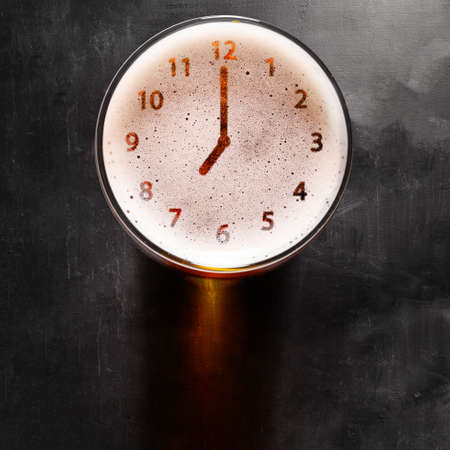 clock symbol on foam in beer glass on black table, view from aboveの写真素材