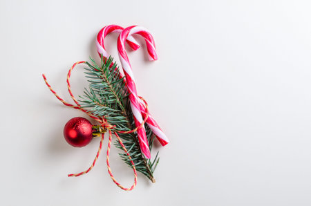 christmas or new year decoration of two candy cones with fir-tree branch and toy glass ball on gray...