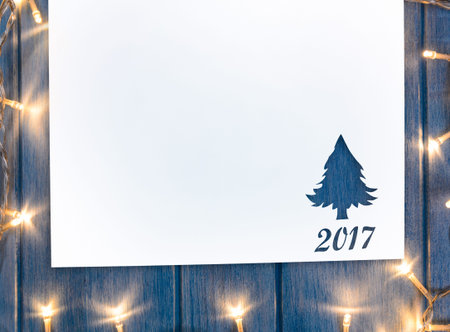 Cut paper in fir-tree shape with decorative lights for christmas card or new year background on blue...