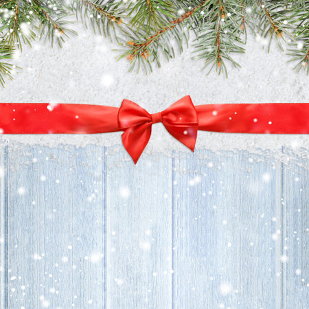 christmas card or new year background made of red satin ribbon with bow on snow and fir-tree branches over blue wooden table