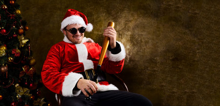 Bad Santa with baseball bat sitting indoors near Christmas or New Year fir treeの写真素材