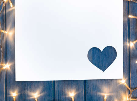 Heart shaped cut paper with decorative lights for Valenine's day greeting card on blue wooden tableの写真素材
