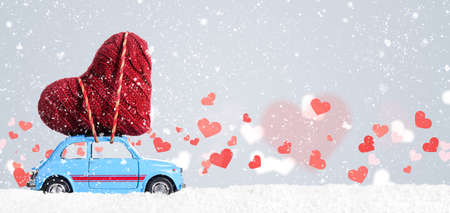 Blue retro toy car delivering heart for Valentine's day on gray backgroundの写真素材