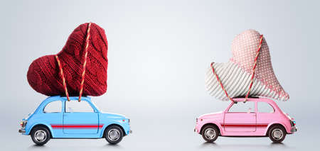 Couple of retro toy cars delivering craft hearts for Valentines day on gray background