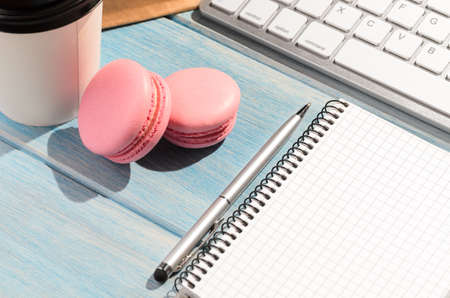 Working on the go. White modern keyboard with coffee cup, candies and notepad on blue wooden table at sunny weatherの写真素材