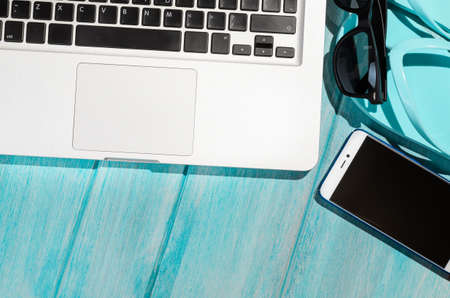 Work on the go. Modern laptop computer with smartphone and sunglasses on blue table, view from aboveの写真素材