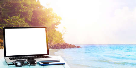 Modern laptop on blue wooden table with blank screen at tropical beachの写真素材