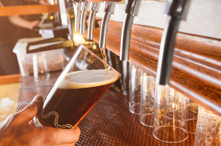 Bartender hand pouring draught beer to glass from a pub tap