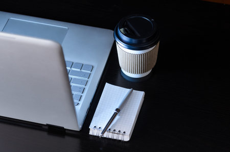 Modern laptop on evening work place, coffee cup and notebook with pen, view from above