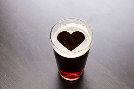 Heart silhouette on foam in beer glass on black table, view from above.の写真素材
