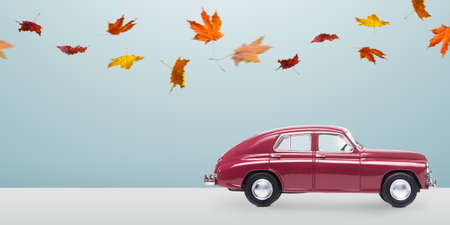 Autumn red toy car with fallen leaves against minimalistic blue backgroundの写真素材