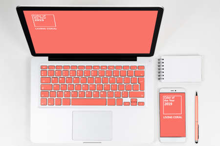 Laptop with living coral colored keyboard with smartphone and notebook, view from aboveの写真素材