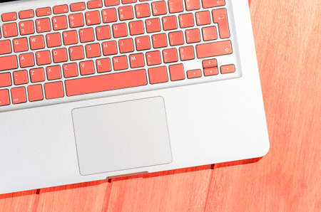 Laptop with living coral colored keyboard on wooden table on a sunny day, view from aboveの写真素材