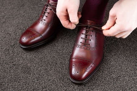 Trying new shoes. Man is putting on a new pair of luxury burgundy full grain leather shoes at footwear storeの写真素材