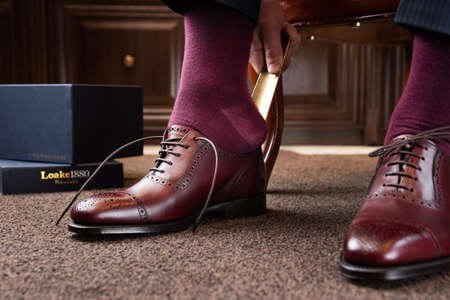 Trying new shoes. Man is putting on a new pair of luxury burgundy full grain leather shoes at footwear storeの写真素材