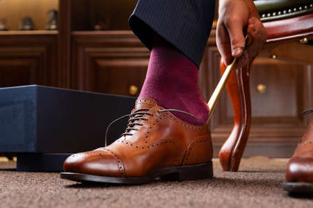 Trying new shoes. Man is putting on a new pair of luxury brown full grain leather shoes at footwear storeの写真素材