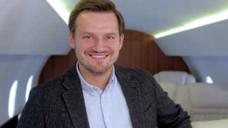 Businessman portrait in private jet. Well dressed, confident male caucasian entrepreneur smiling inside of business airplane cabin.の写真素材