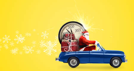 Christmas countdown arriving. Santa Claus on snowy toy car delivering New Year gifts and clock at yellow backgroundの写真素材