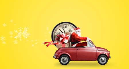 Christmas countdown arriving. Santa Claus on snowy toy car delivering New Year gifts and clock at yellow backgroundの写真素材