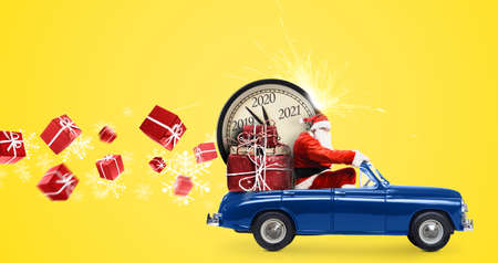 Christmas countdown arriving. Santa Claus on snowy toy car delivering New Year gifts and clock at yellow backgroundの写真素材