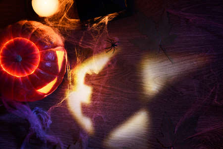 Projection of Halloween pumpkin lantern with Jack oLantern face on table with fallen autumn leaves and candles. Top view.の写真素材