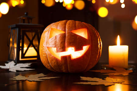 Halloween pumpkin lantern on table with Jack oLantern face with fallen autumn leaves and candles.の写真素材