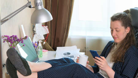 Woman working on phone and laptop from home due to coronavirus self isolation. Authentic home workplace. Coronavirus outbreak 2020.の写真素材