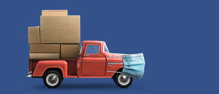 Safe delivery. Toy car in mask delivering blank boxes. Loaded red pickup truck with protection on blue backgroundの写真素材