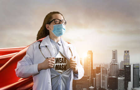 Medical superhero showing stay home caption. Heroic doctor wearing mask and red cape fighting with epidemic in city and promoting stayhome movement. Young woman. Brave medical staff concept.の写真素材
