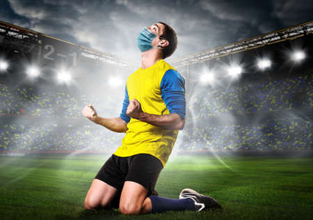 Soccer or football player wearing mask. Team sports player in medical mask emotionally kneel on stadium during coronavirus outbreak.