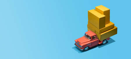 Fast order delivery by car concept. Pickup truck delivering blank boxes. Loaded retro toy car loaded with cardboard packages isolated on blue background.の写真素材