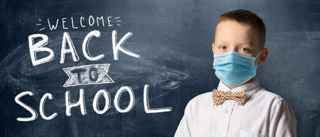 School boy wearing face mask standing against blackboard. Safe back to school during pandemic concept. New normal education.の写真素材