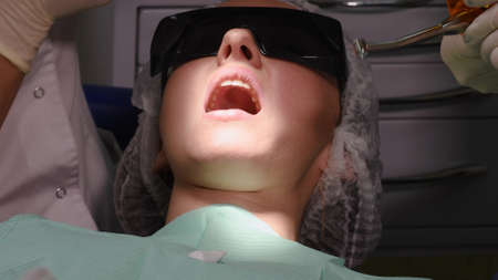 Curing dental resin based composite in tooth with LED. Young woman at dental clinic. Female dentist with assistant treating cavities in a patient mouth in modern dental office.の写真素材