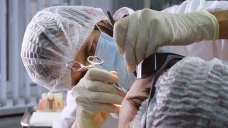 Suturing stitches. Oral surgeon performing surgery installing implant into senior woman mouth. Dentist works with a patient in modern dental clinicの素材 [FY310151033243]