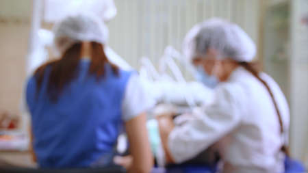 Young woman at dental clinic. Female dentist with assistant treating cavities in a patient mouth in modern dental office. Handheld shot with gimbal. Out of focus for background use.の写真素材