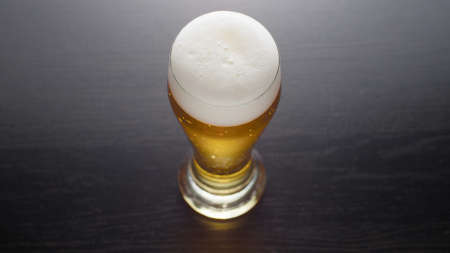 Glass of frothy fresh beer on tableの写真素材
