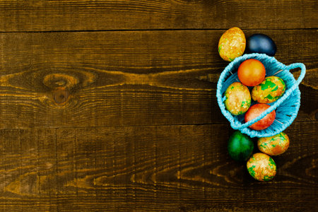Blue basket with Easter eggs and Easter eggs lying nearby on the dark brown wooden background, copy spaceの写真素材