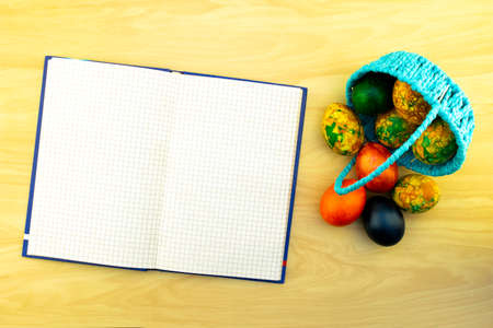 Easter eggs lying in the blue basket and on a yellow wooden table, a book for notes as a copy of pastesの写真素材
