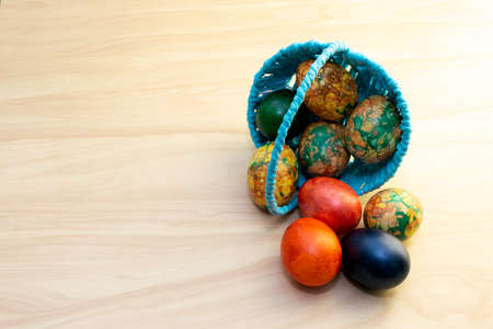 Easter eggs lying on the yellow wooden table and in a blue basket, copy pastesの写真素材