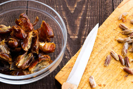 Hushaf - date milk, traditional Ramadan dish, cooking, ingredients, pitted dates in a plate, knife and seeds on a cutting board on the wooden tableの写真素材