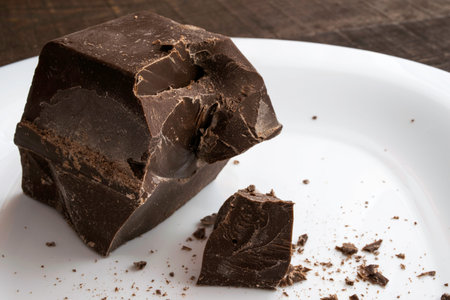 a large chopped piece of chocolate on a white ceramic plate stands on a brown wooden table