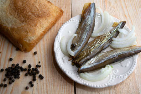 smoked capelin on a dish stands on a wooden table with a piece of bread and pepperの写真素材