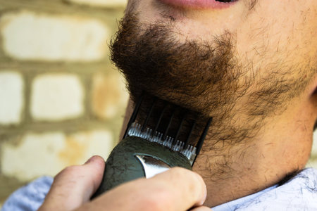 the barber cuts his beard to the guy with a shearing machineの写真素材